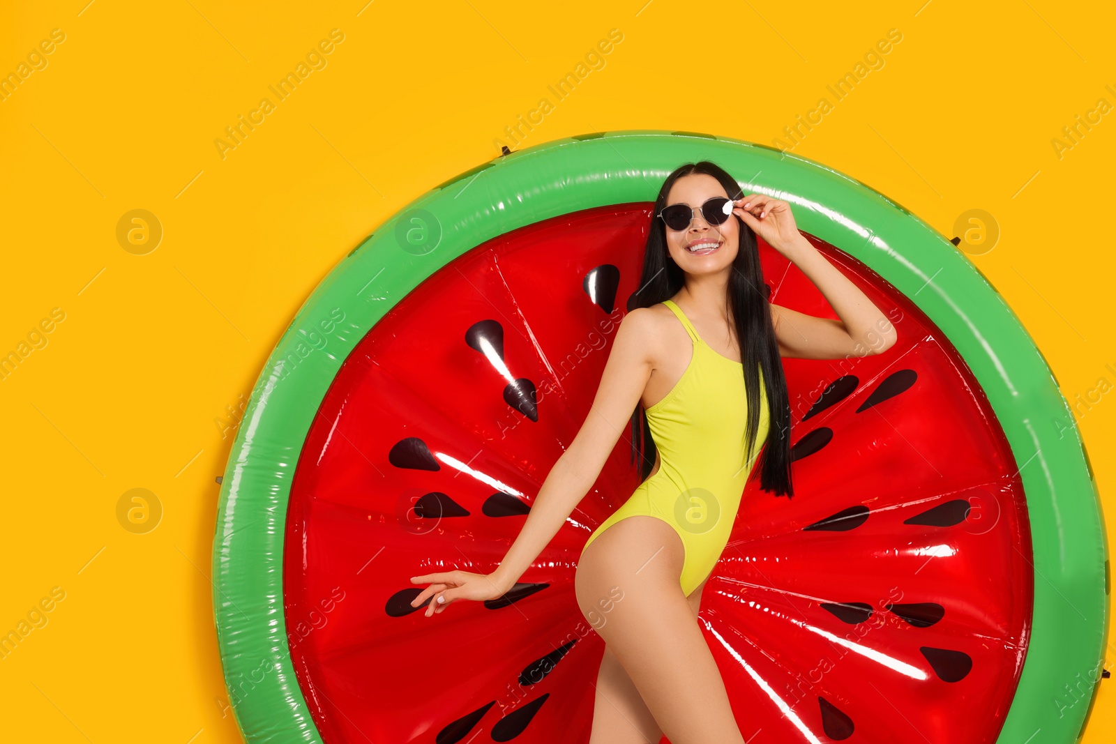 Photo of Young woman with stylish sunglasses near inflatable mattress against orange background