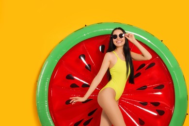 Young woman with stylish sunglasses near inflatable mattress against orange background