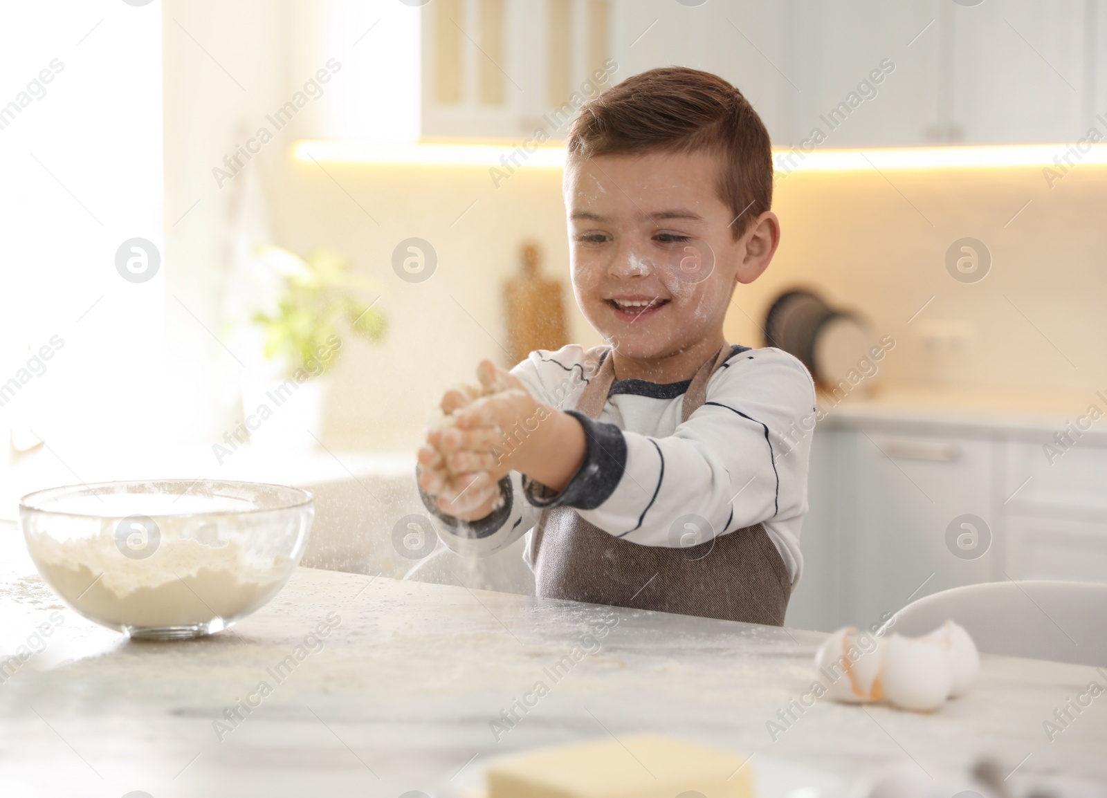 Photo of Cute little boy cooking dough at table in kitchen