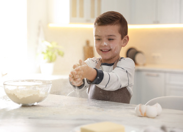 Cute little boy cooking dough at table in kitchen