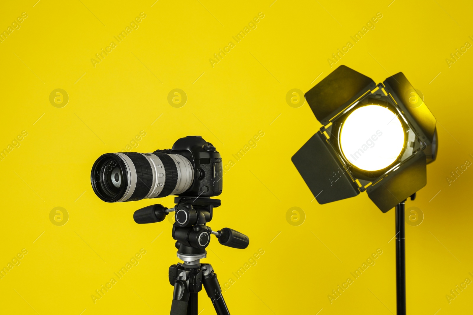 Photo of Professional video camera and lighting equipment on yellow background