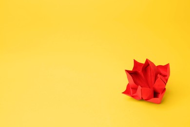 Origami art. Handmade red paper flower on yellow background, space for text