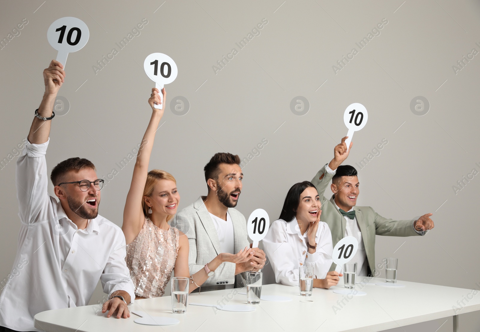 Photo of Panel of judges holding signs with highest score at table on beige background