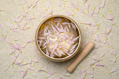 Photo of Tibetan singing bowl with water, petals and mallet on beige table, top view