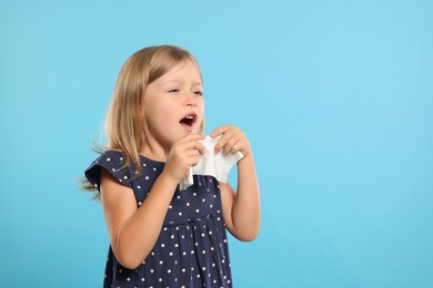 Suffering from allergy. Little girl with tissue sneezing on light blue background, space for text