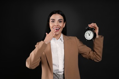Photo of Emotional businesswoman holding alarm clock on black background. Time management