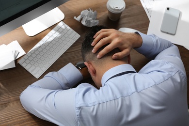 Stressed out businessman at workplace in office, above view