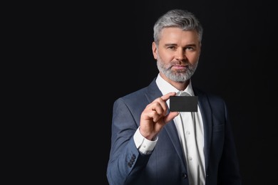 Handsome businessman holding blank business card on black background. Space for text