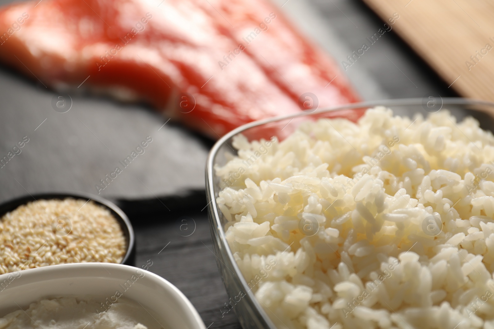 Photo of Cooked rice in bowl and other ingredients for sushi on table, closeup