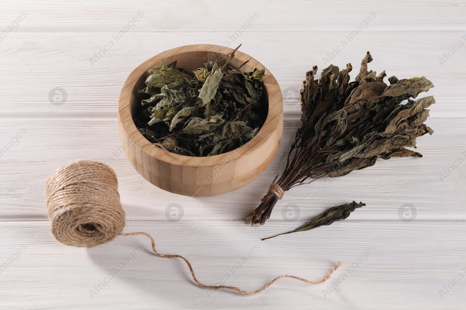 Photo of Bowl with dry basil and spool of twine on white wooden table