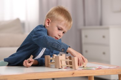 Photo of Cute little boy playing with set of wooden animals and fence at table indoors, space for text. Child's toy