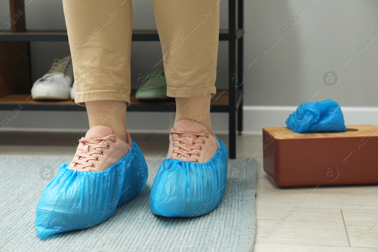 Photo of Woman wearing blue shoe covers onto her sneakers indoors, closeup