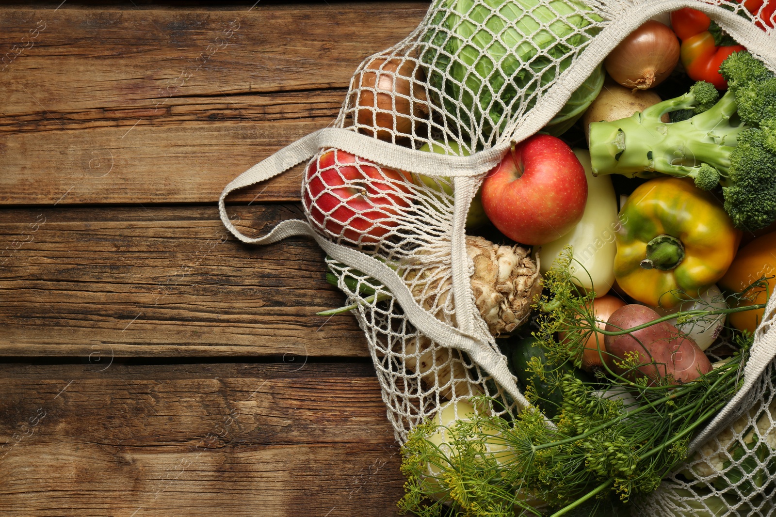 Photo of Different fresh vegetables in net bag on wooden table, top view with space for text. Farmer harvesting