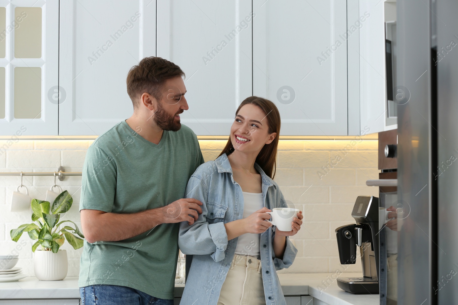 Photo of Happy couple preparing fresh aromatic coffee with modern machine in kitchen