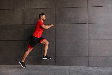 Happy man running near building outdoors. Space for text