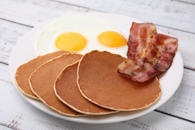 Tasty pancakes with fried eggs and bacon on white wooden table, closeup