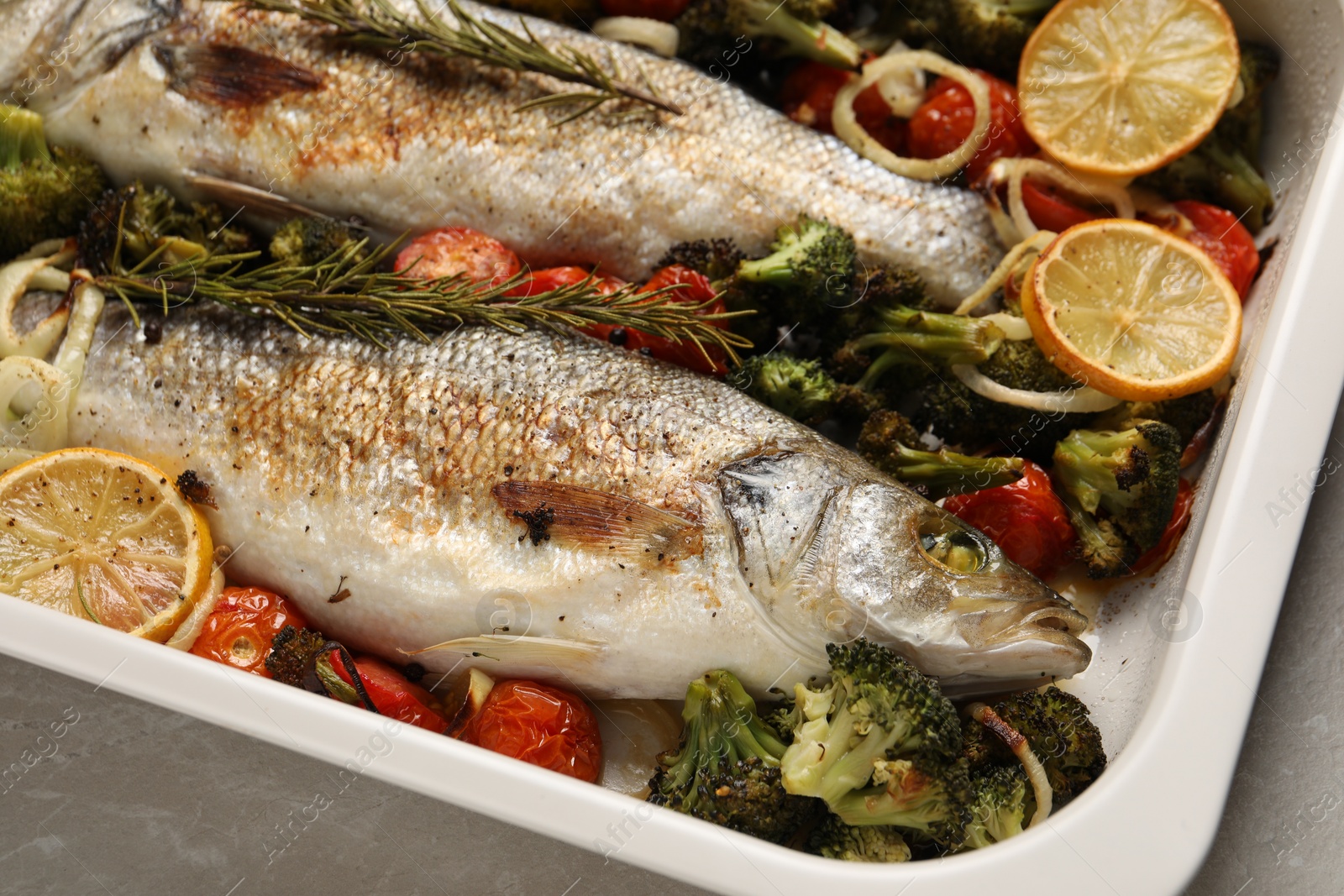 Photo of Delicious fish with vegetables and lemon in baking dish on light marble table, closeup