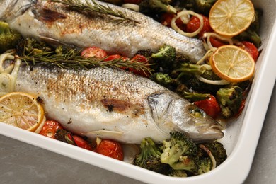 Delicious fish with vegetables and lemon in baking dish on light marble table, closeup