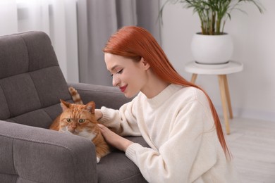 Woman stroking her cute cat in armchair at home