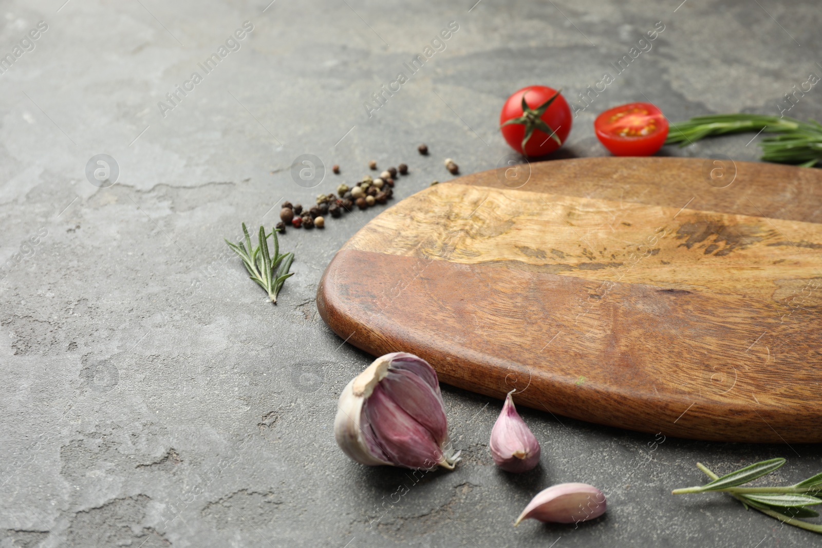 Photo of Cutting board, rosemary, garlic, pepper and tomatoes on black table. Space for text