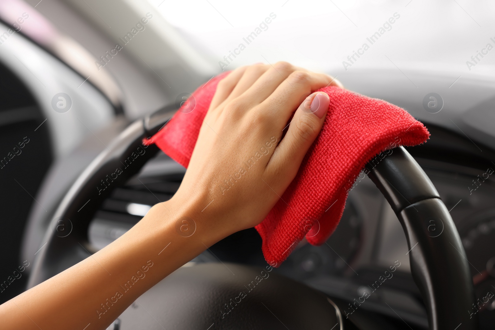 Photo of Woman cleaning steering wheel with rag in car, closeup