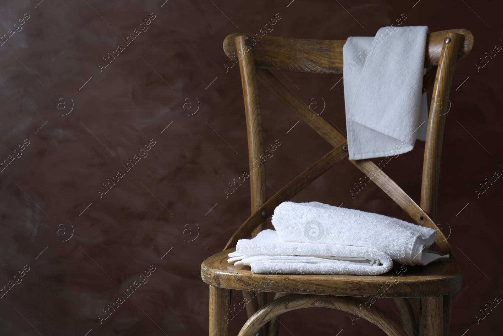 Photo of White terry towels on wooden chair against brown background. Space for text