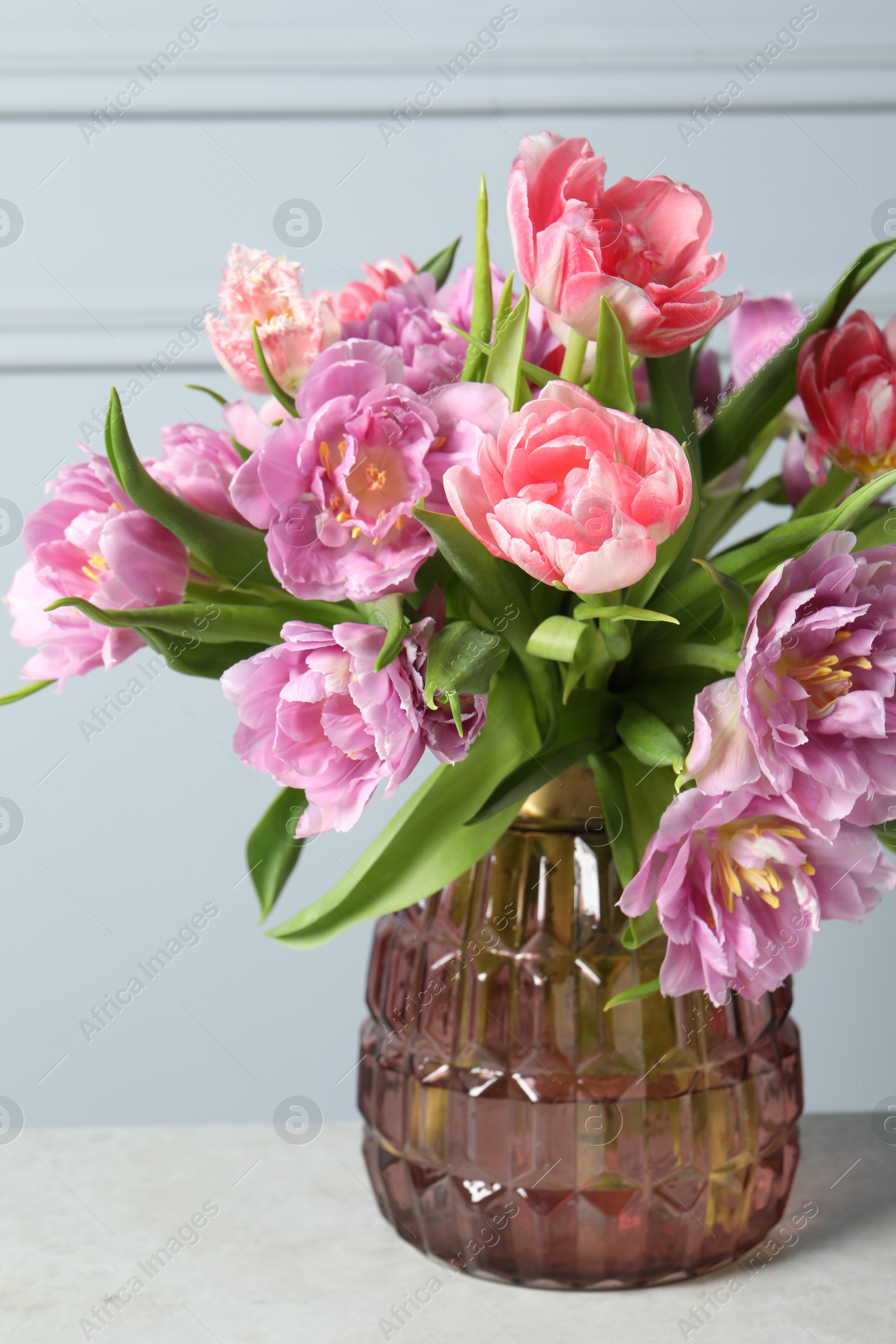 Photo of Beautiful bouquet of colorful tulip flowers on white table near light grey wall