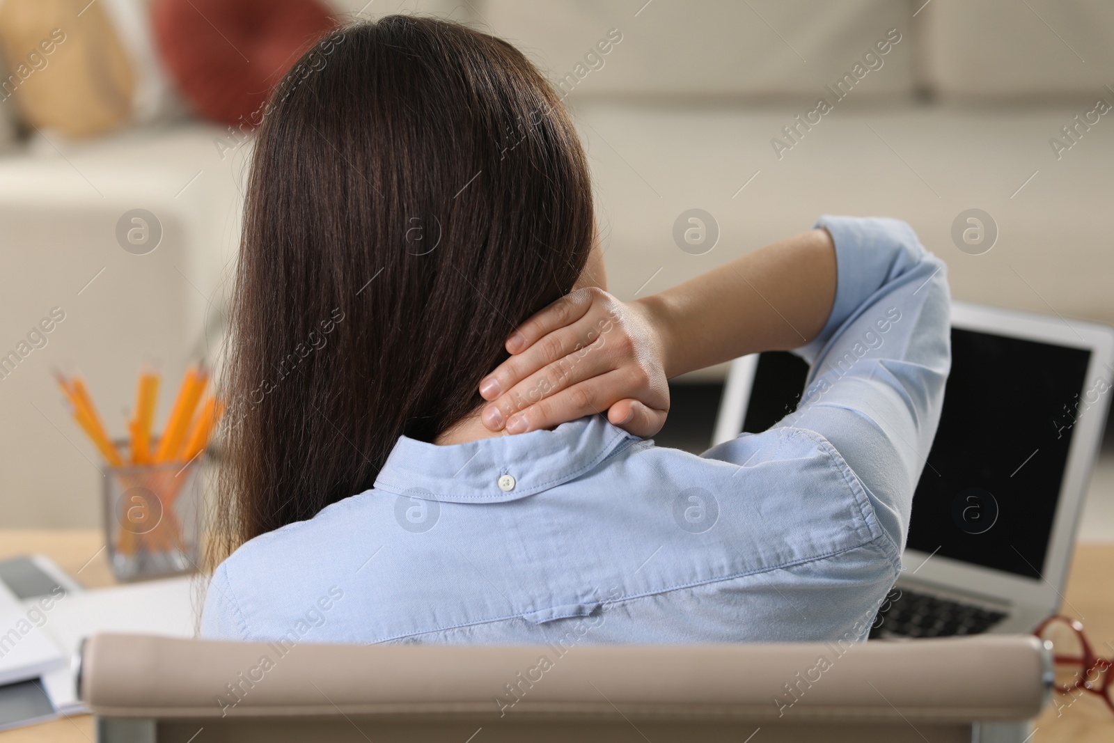 Photo of Woman suffering from neck pain at table in office, back view