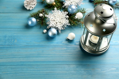 Photo of Christmas lantern with burning candle and festive decor on light blue wooden table. Space for text