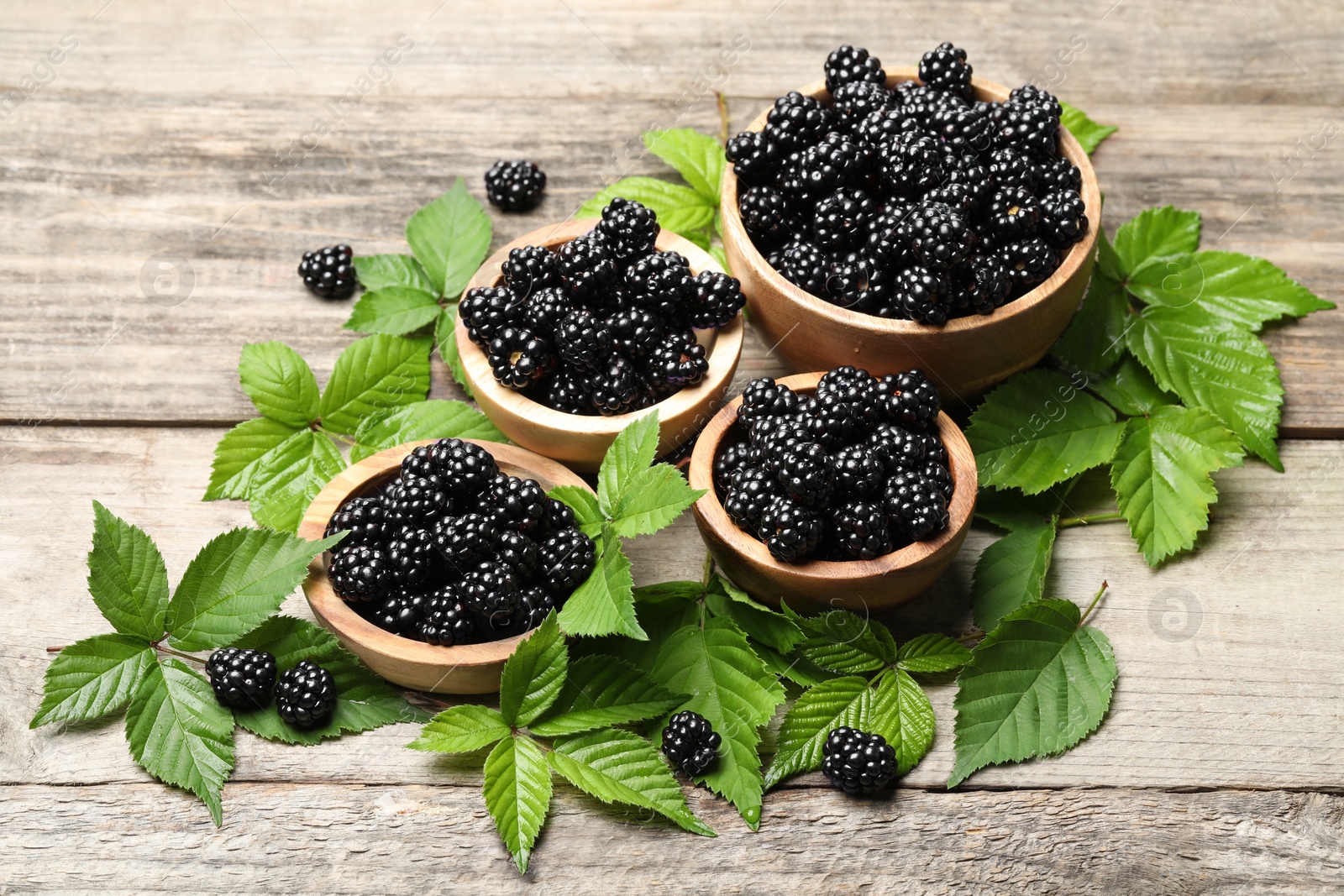 Photo of Ripe blackberries and green leaves on wooden table