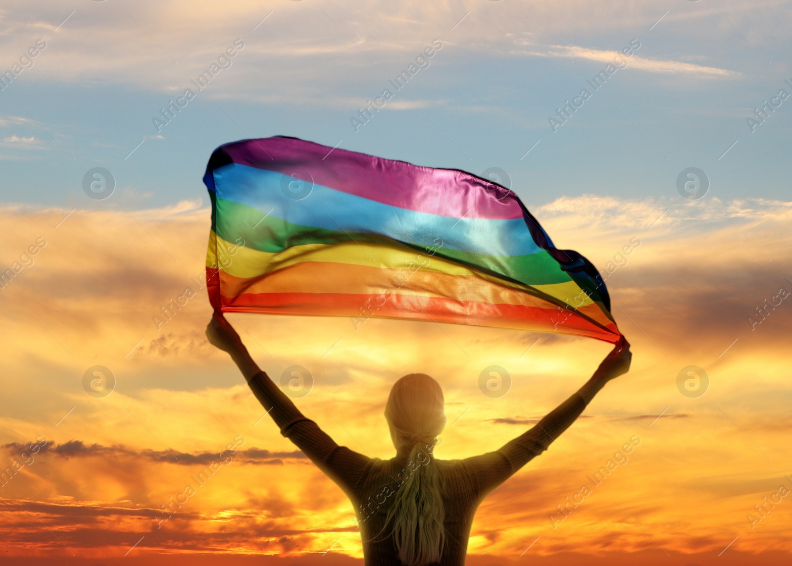 Image of Woman with bright LGBT flag against sky at sunset