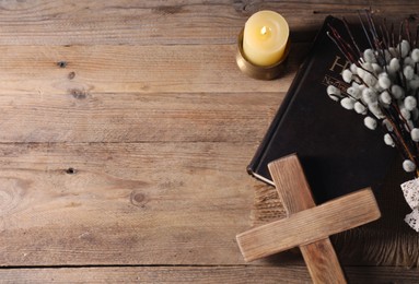 Photo of Burning church candle, cross, Bible and willow branches on wooden table, flat lay. Space for text