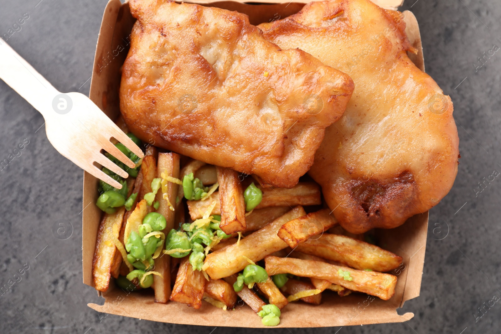 Photo of Tasty fish, chips and peas in paper box on grey table, top view