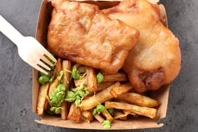 Photo of Tasty fish, chips and peas in paper box on grey table, top view