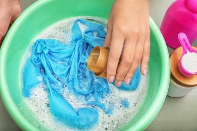 Photo of Woman adding detergent into basin with color clothes, top view