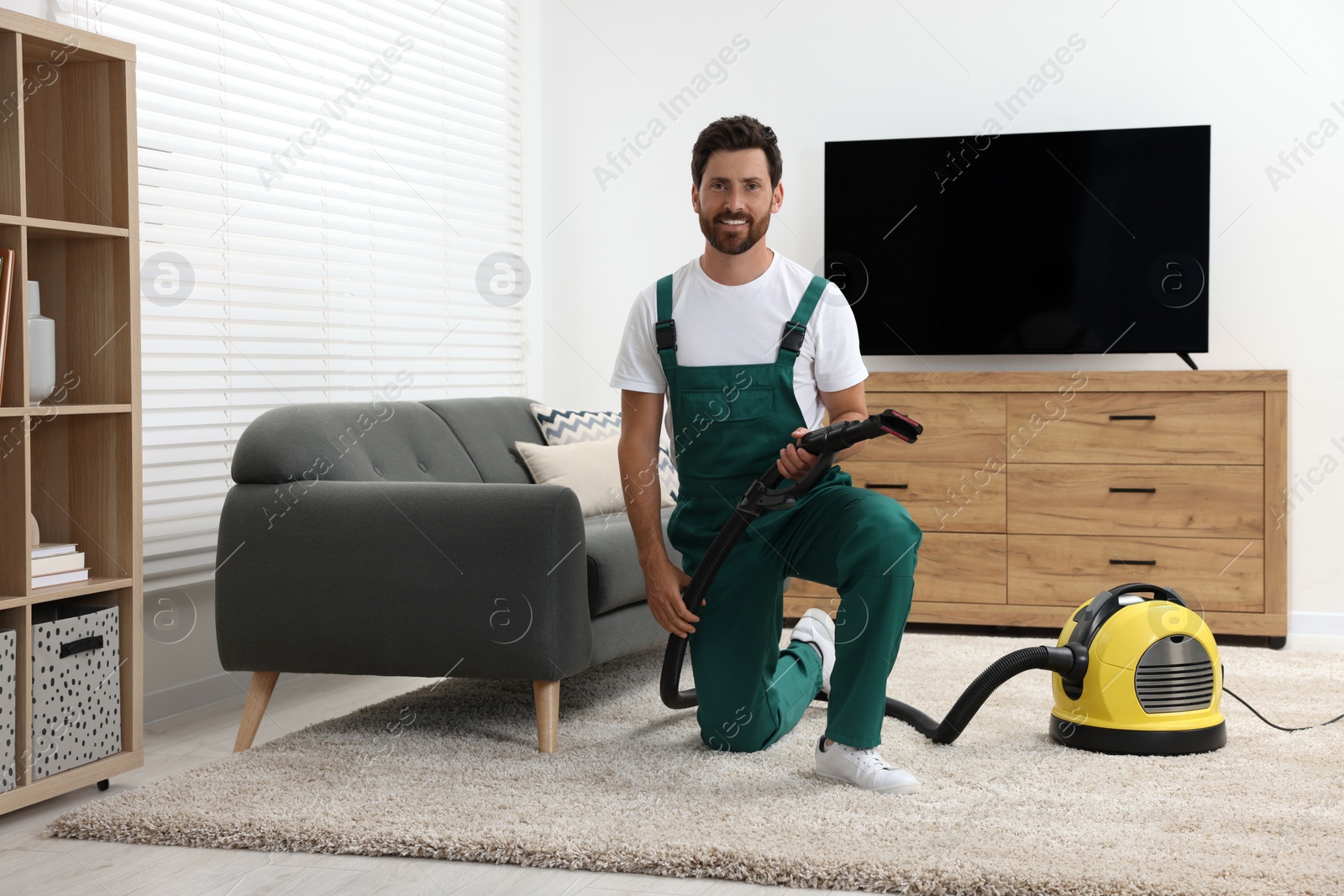 Photo of Dry cleaner's employee with vacuum cleaner on carpet in room