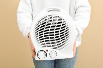 Photo of Young woman holding electric fan heater on beige background, closeup