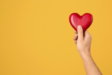 Man holding decorative heart in hand on color background, space for text