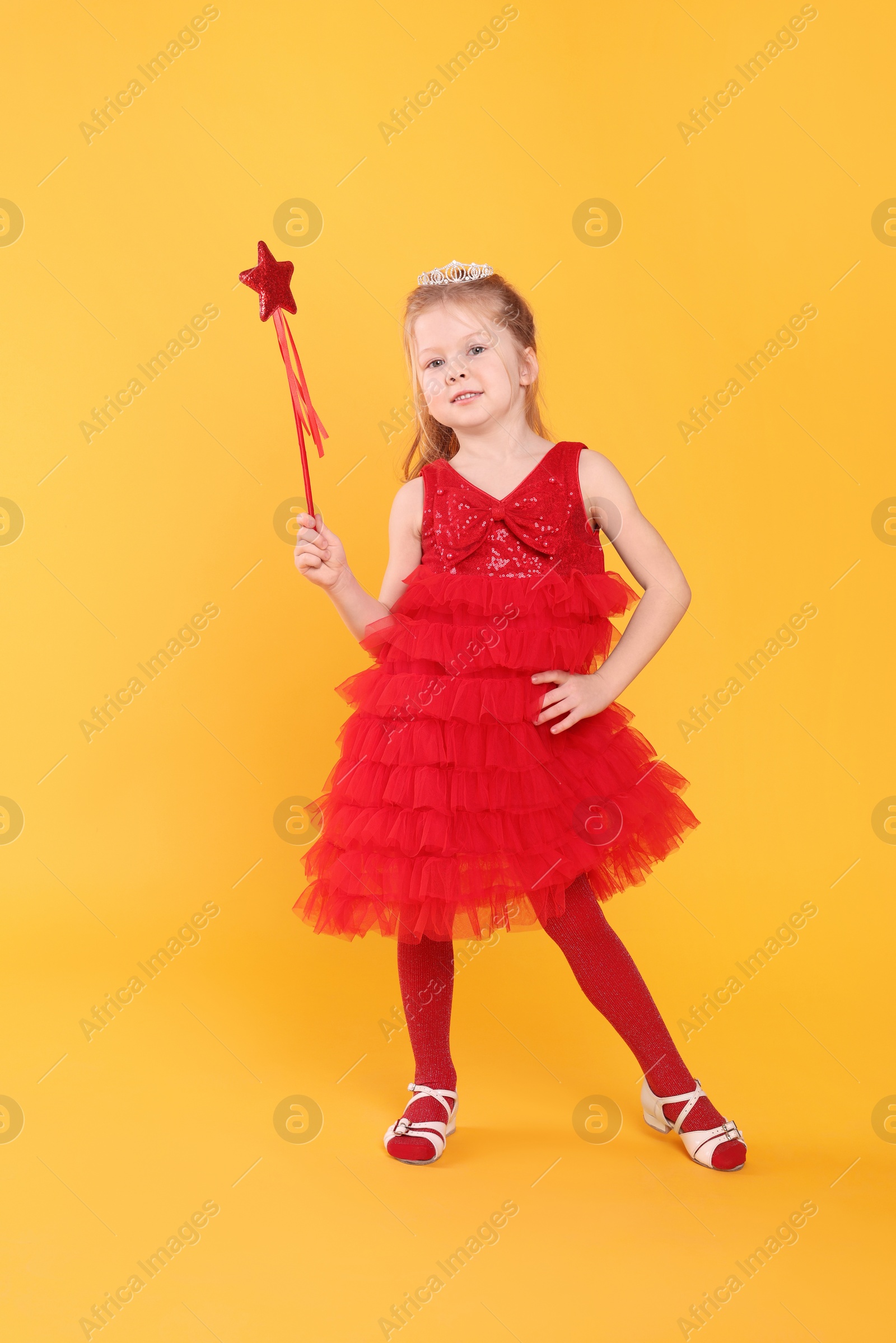 Photo of Cute girl in red dress with diadem and magic wand on yellow background. Little princess