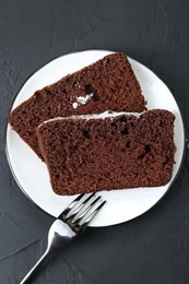 Photo of Pieces of tasty chocolate sponge cake with powdered sugar on black textured table, top view