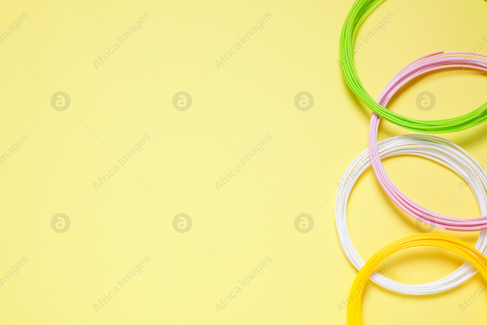 Photo of Colorful plastic filaments on pale yellow background, flat lay. Space for text