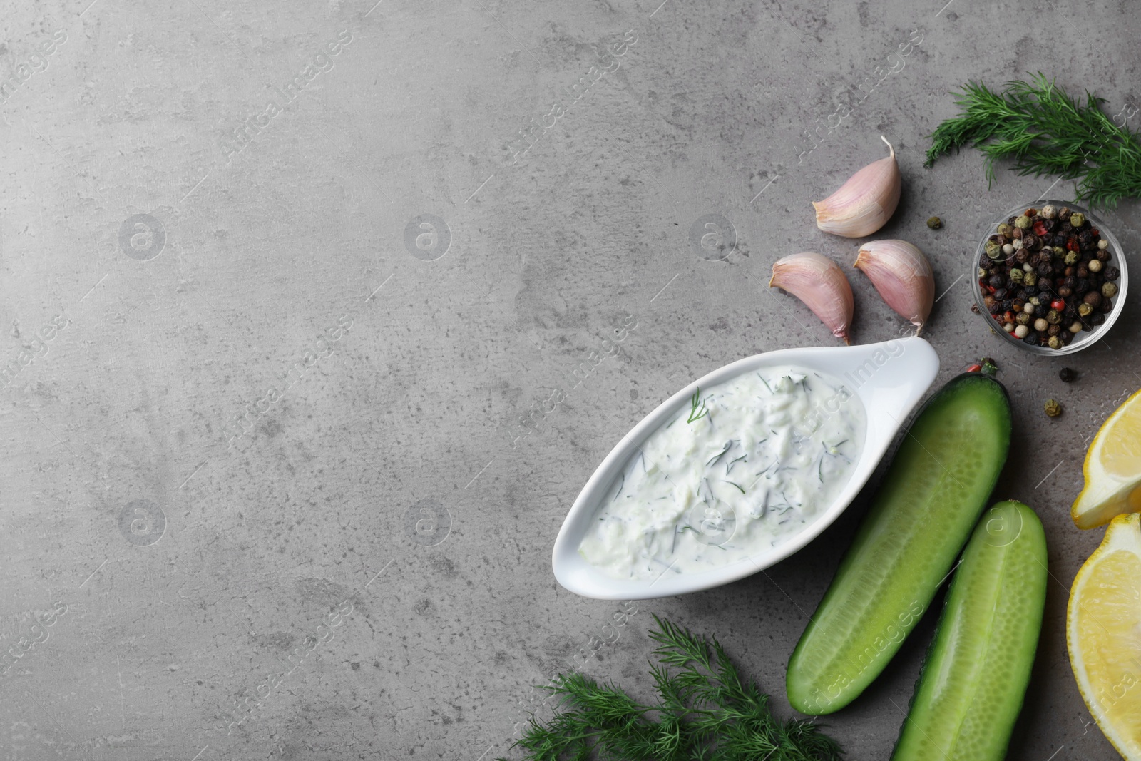 Photo of Tzatziki cucumber sauce with ingredients on grey background, top view. Space for text