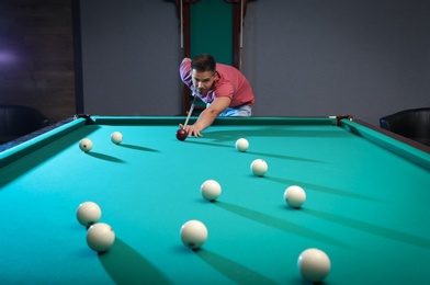 Photo of Handsome young man playing Russian billiard indoors