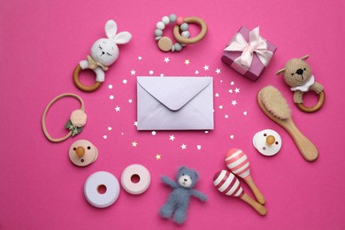 Photo of Baby shower party. Envelope surrounded by gift box, toys and accessories for child on bright pink background, flat lay