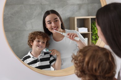 Mother and her son brushing teeth together near mirror in bathroom