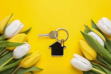 Photo of Beautiful spring flowers and key with trinket in shape of house on yellow background, flat lay