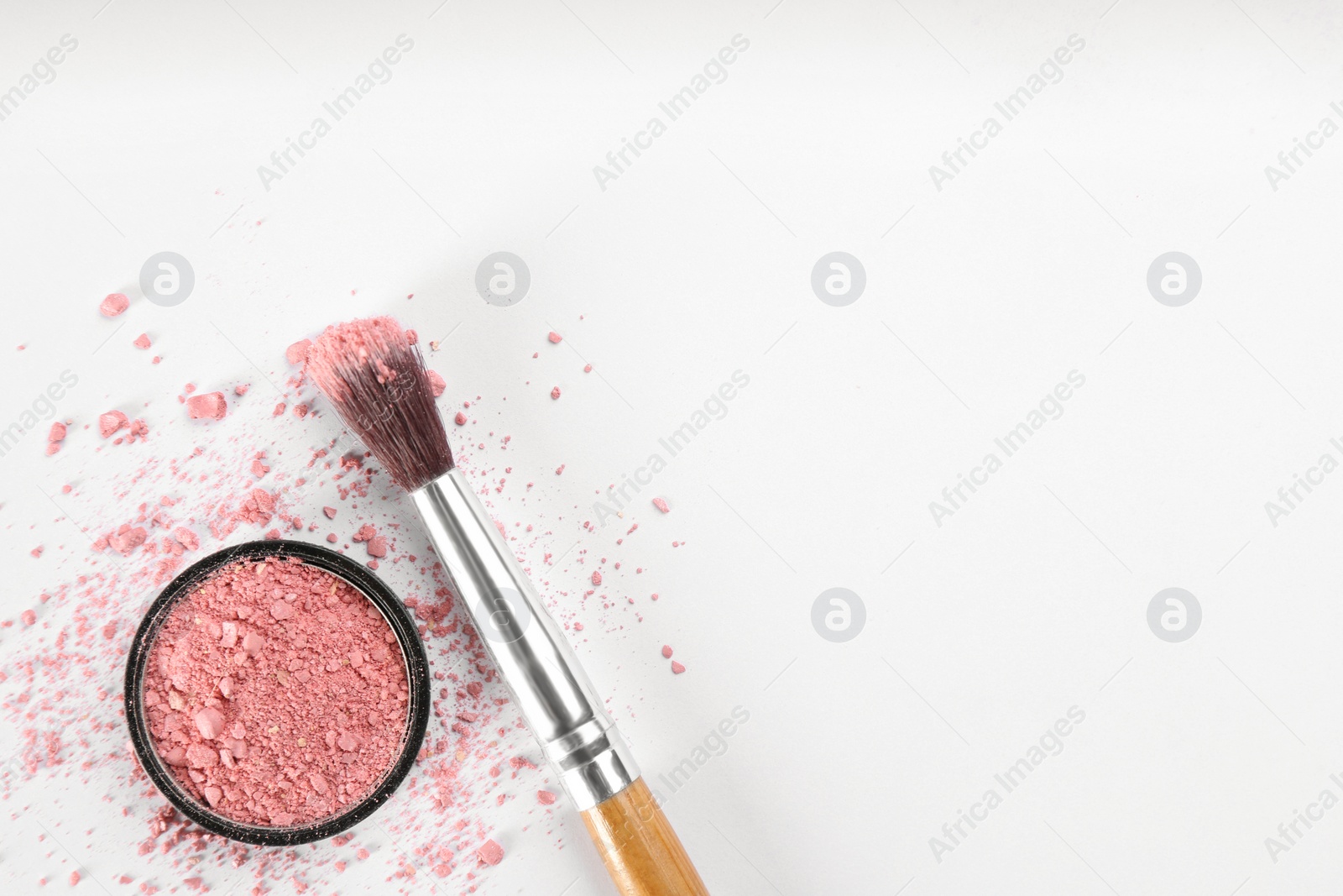 Photo of Makeup brush and scattered blush on white background, top view. Space for text