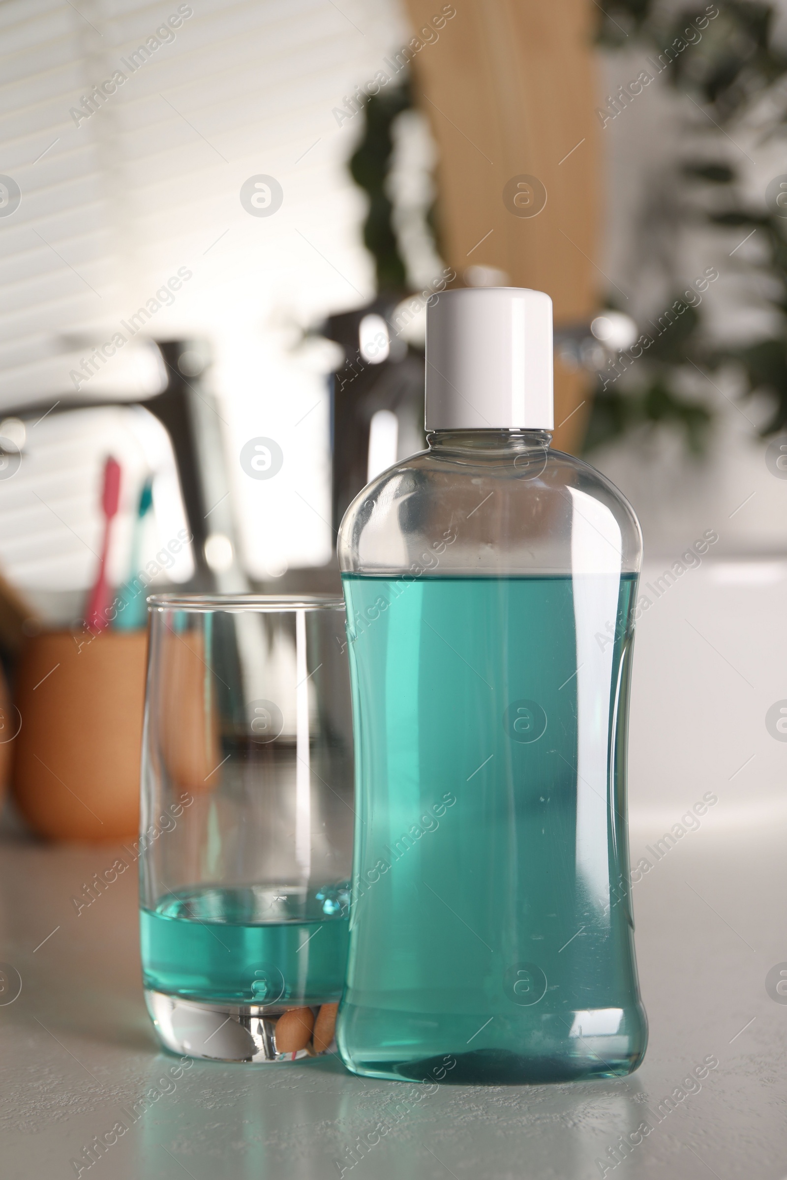 Photo of Bottle and glass of mouthwash on light table in bathroom