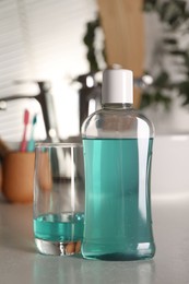 Photo of Bottle and glass of mouthwash on light table in bathroom