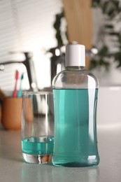 Bottle and glass of mouthwash on light table in bathroom